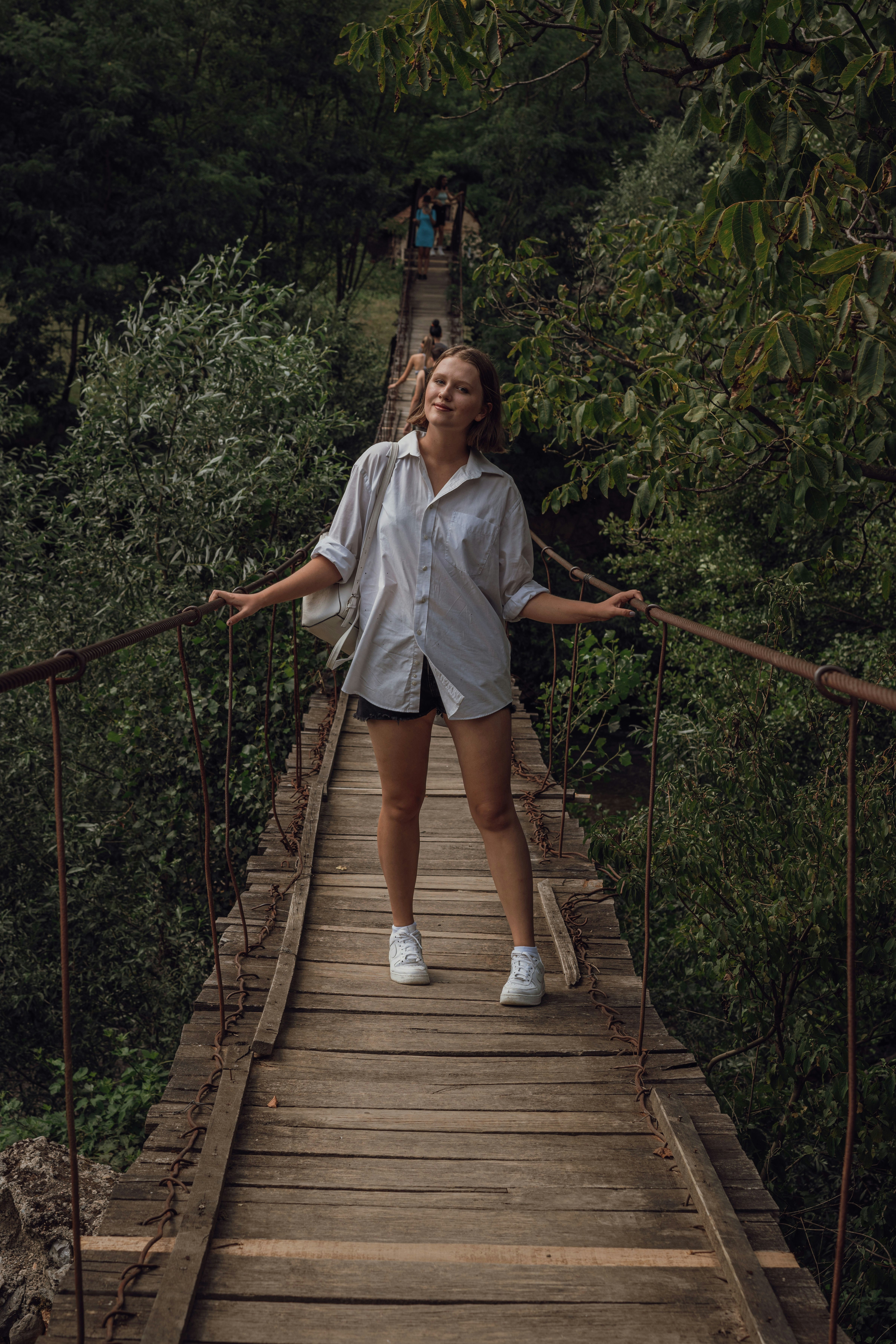 woman in gray shirt and brown shorts standing on hanging bridge
